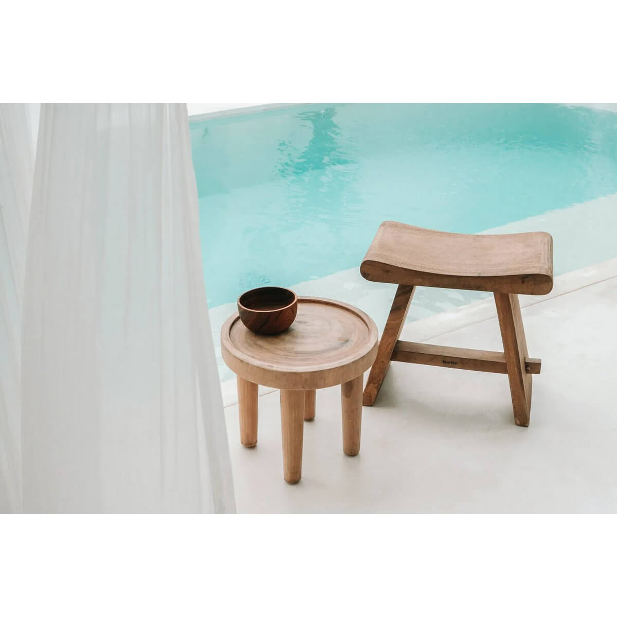 Teak wooden table and stool set by a poolside, featuring a rustic bohemian style, perfect for outdoor relaxation.