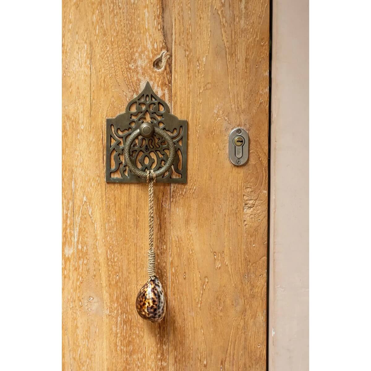 Bohemian Tranquility Tassel with unique 'tiger' shell hanging on a rustic door, adding exotic flair to home decor.