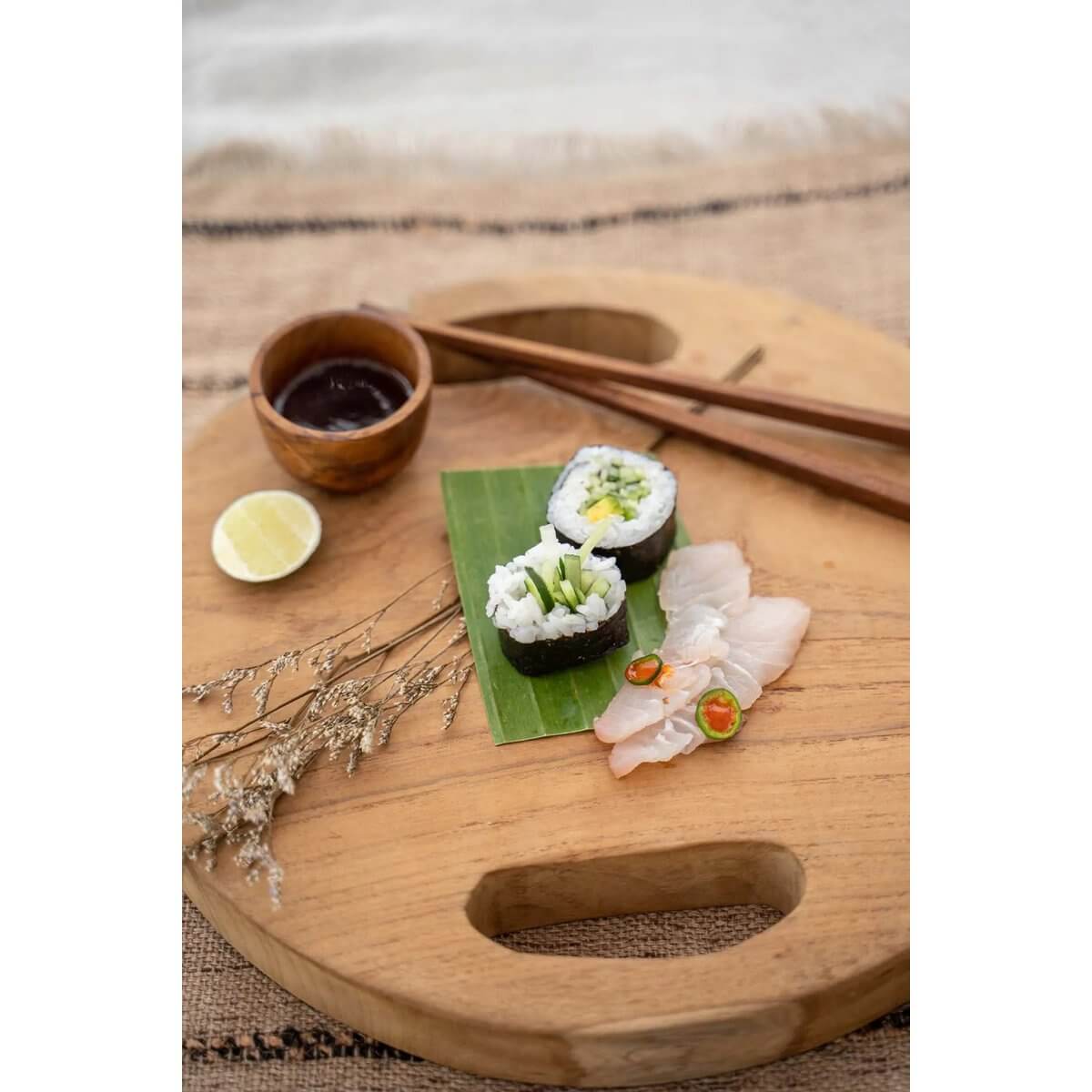 Teakhouten snijplank met sushi en sojasaus, gebruikt als stijlvol dienblad op een aanrecht.