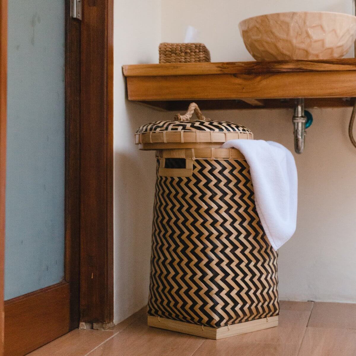 Decoratieve bamboe wasmand Nabire met deksel, tweekleurig zigzag-design, in badkamer geplaatst.