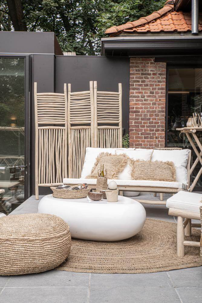 Zeegras vloerkleed op overdekt terras met natuurlijke decoratie, witte bank en ronde tafel, ideaal voor rustieke sfeer en comfort.