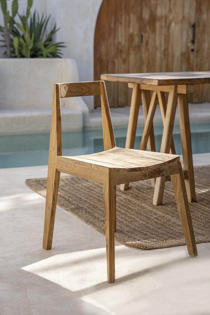Handgemaakte De Paxi Stoel van gerecycled teakhout, ontworpen voor buitengebruik, op een zonnig terras bij een zwembad.