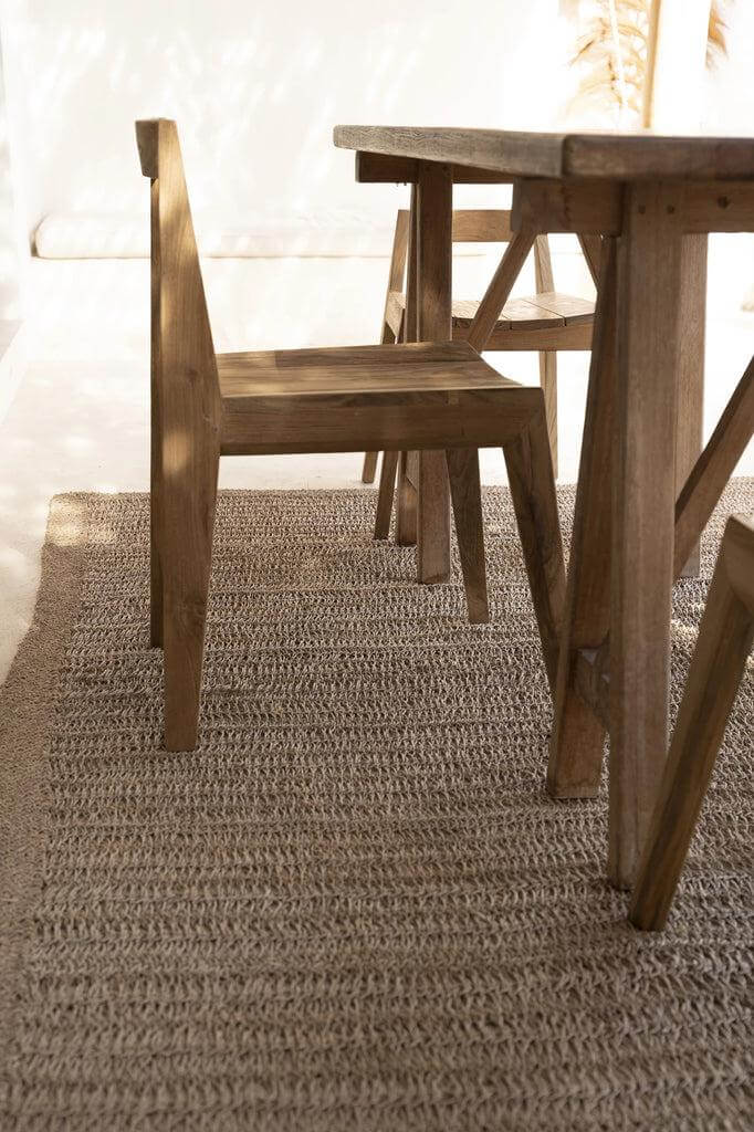 Natuurlijke De Paxi Stoel van gerecycled teakhout voor buitengebruik, met een duurzame en tijdloze uitstraling op geweven tapijt.
