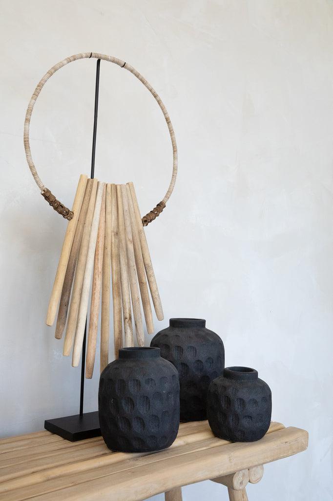 Kunstwerk van drijfhoutstokken op standaard, met zwart getextureerde vazen op houten tafel voor een natuurlijk interieuraccent.