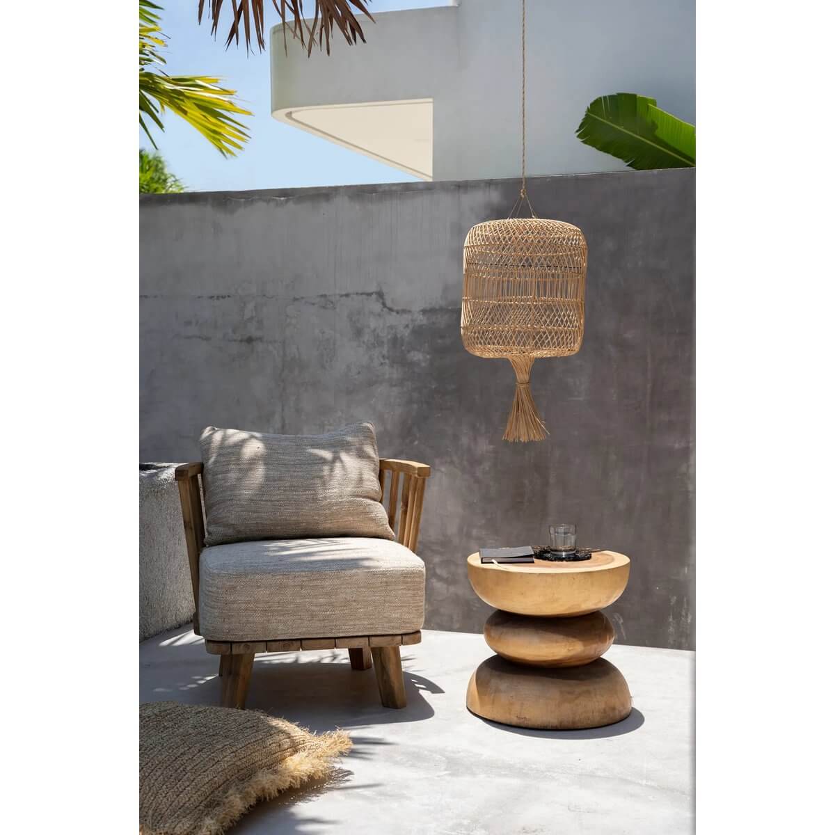 Rotan en bamboe Dumpling hanglamp boven een boho loungehoek met stoel en houten tafel buiten.