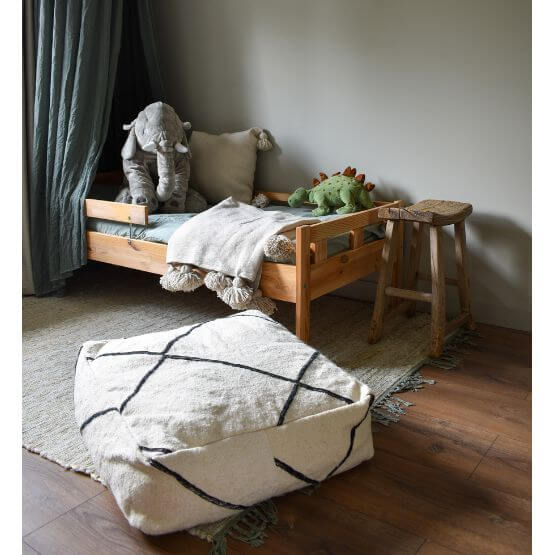 Sfeervol interieur met Beni Ouarain vloerkussen en houten kinderbed, omringd door knuffels in een gezellige kamer.