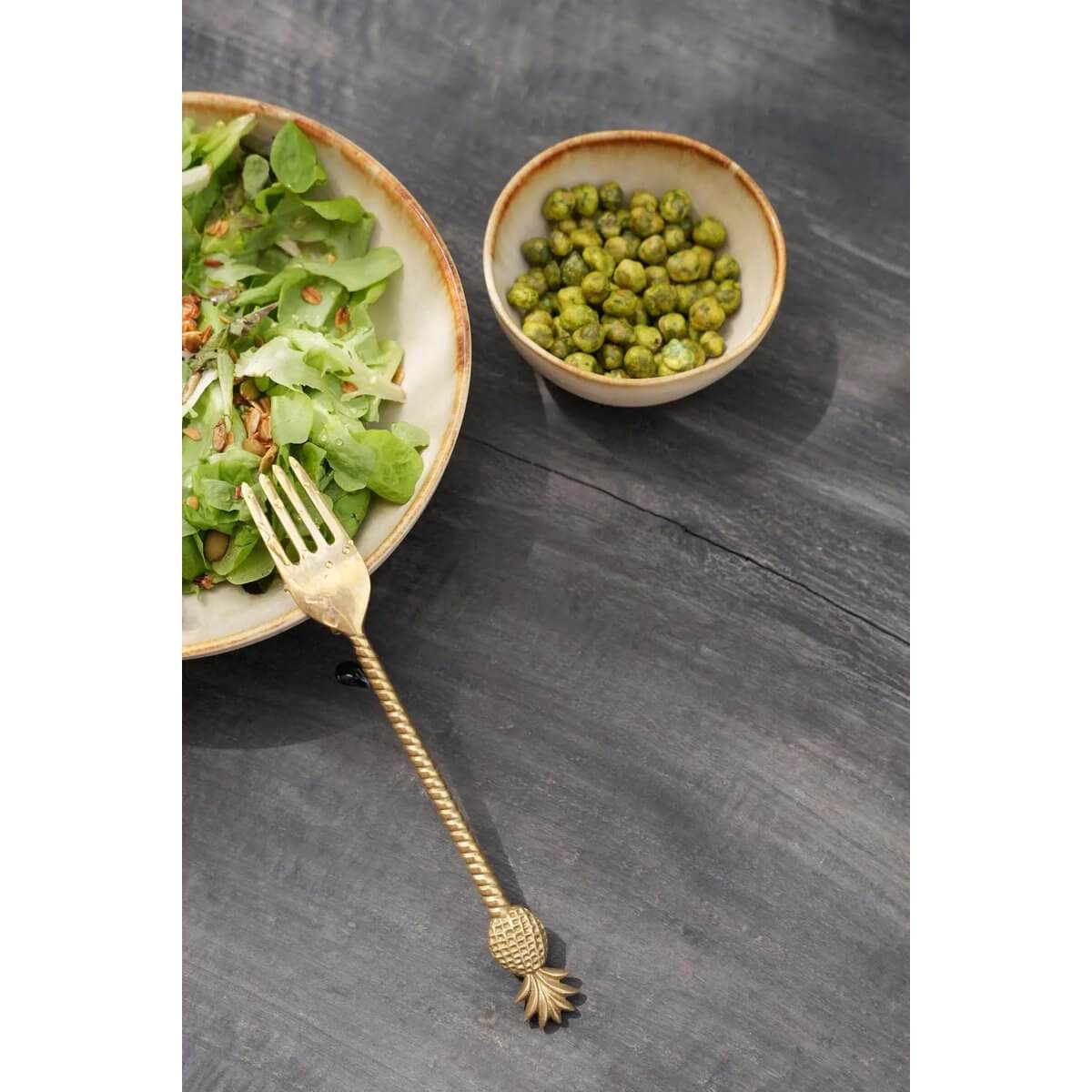 Bohemian gold pineapple fork next to a fresh salad and peas, showcasing the luxurious Ananasvork cutlery collection.