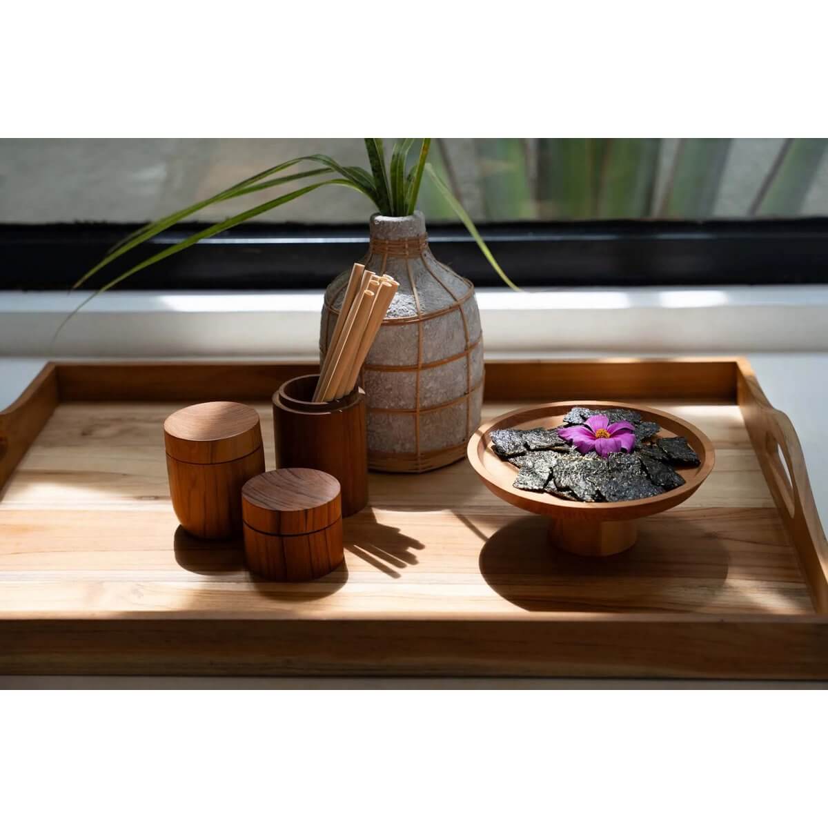 Bohemian bamboo tray with decorative vase, eco-friendly wooden containers, and dried leaves in a cozy sunlight setting.
