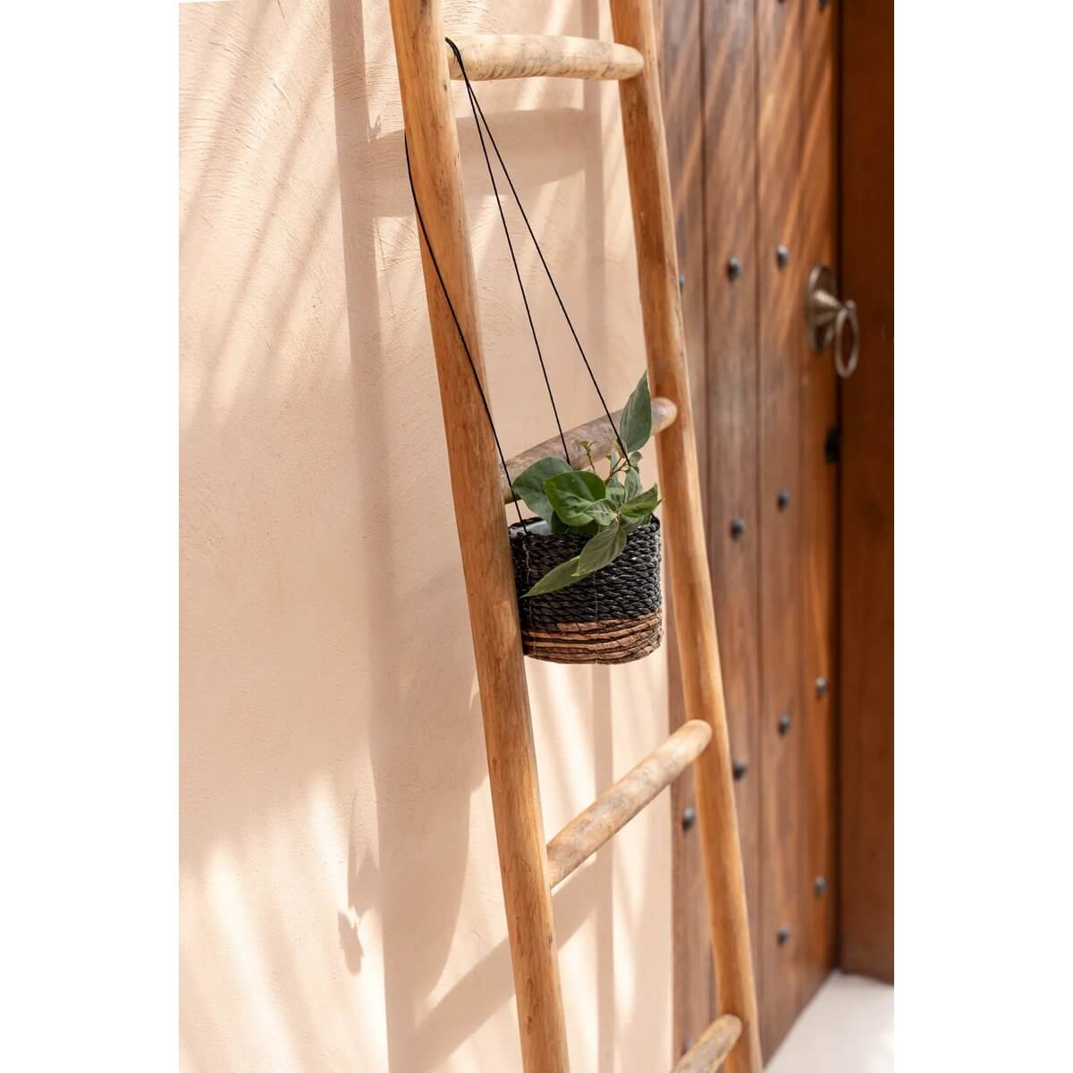 Bohemian style banana leaf and seagrass hanging plant holder in natural black on wooden ladder, ideal for indoor decor.