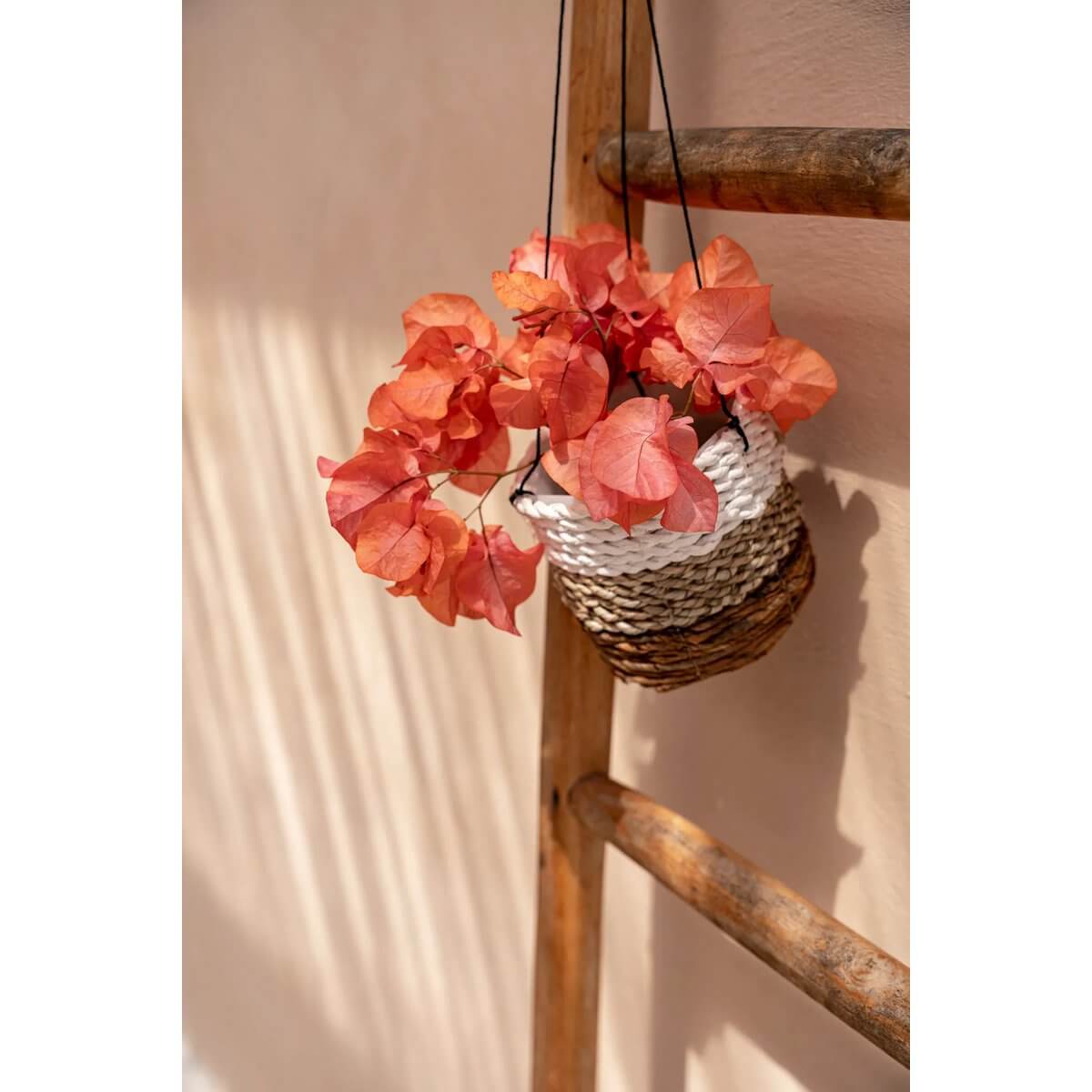 Bohemian De Bananenplanthanger in naturel wit, filled with vibrant orange faux bougainvillea, hangs on wooden ladder. Perfect for indoors.
