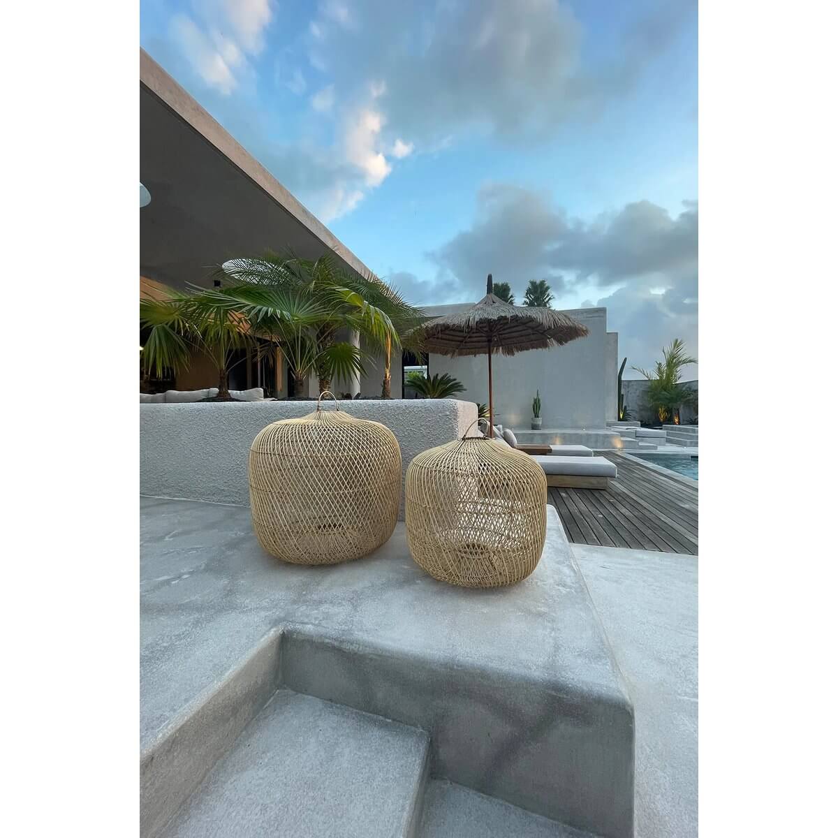 Bohemian style De Batu Bolong lampenkap hangers on modern patio steps, showcasing natural rattan artistry against a serene pool backdrop.