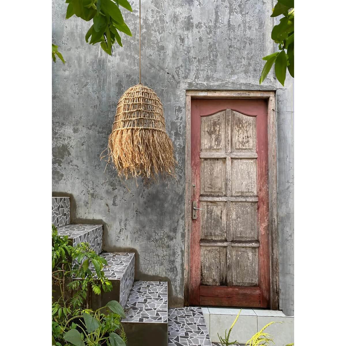 Bohemian De Casita hanging lamp in natural mendonggras, creating tropical vibes by a rustic door. Ideal for indoor and outdoor spaces.