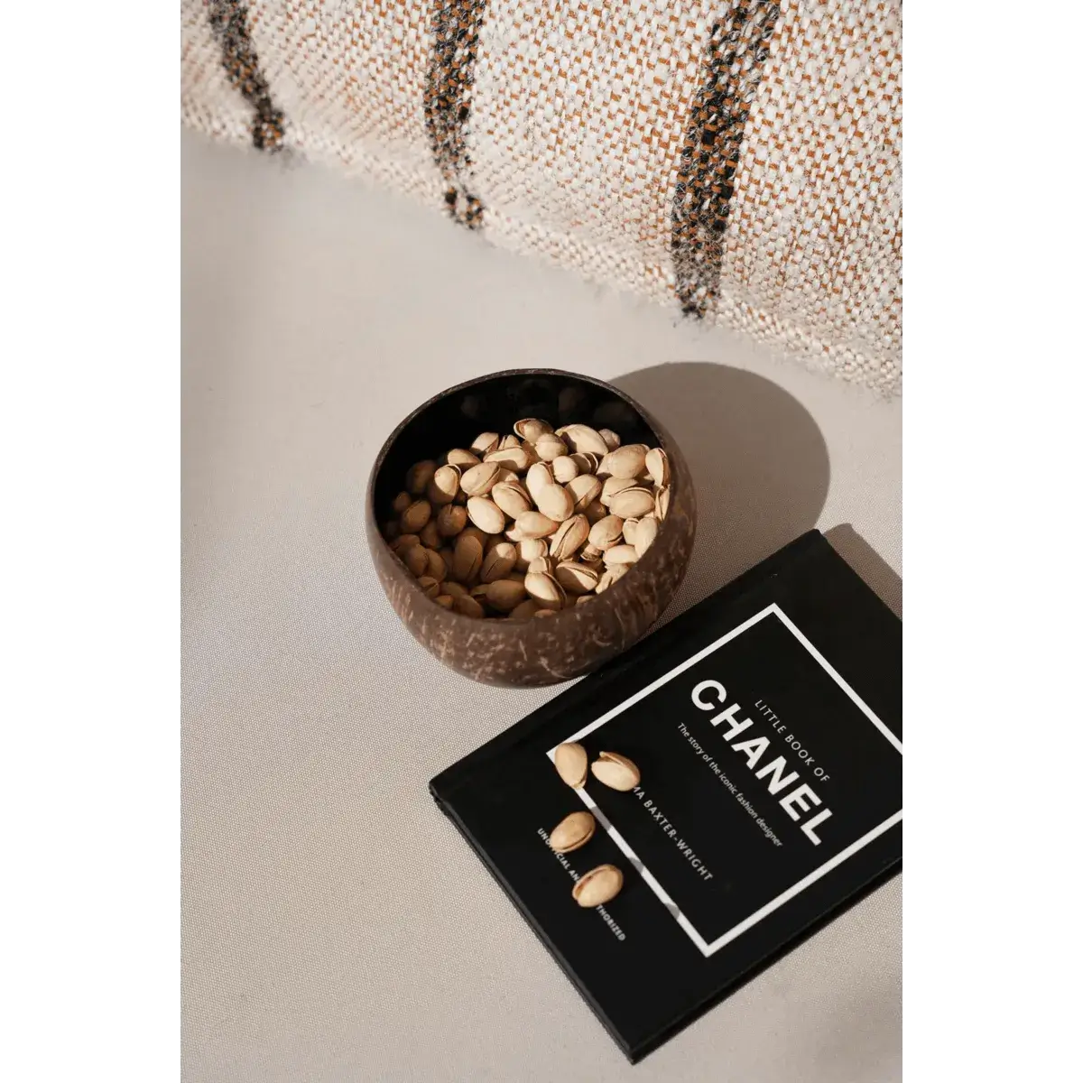 Bohemian style coconut bowl filled with pistachios next to a book on a cozy surface.