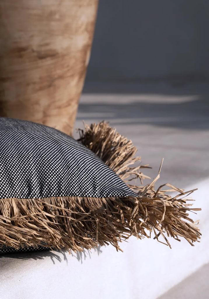 Stijlvolle kussenhoes De Cotton Bonita zwart-wit met raffia franjes, ideaal voor een 'coastal' touch in huis of tuin.