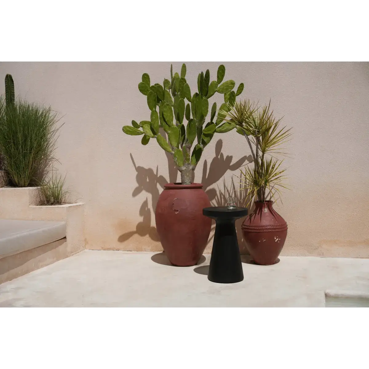 Bohemian style black Fiji side table next to terracotta pots with green plants on a sunlit patio.