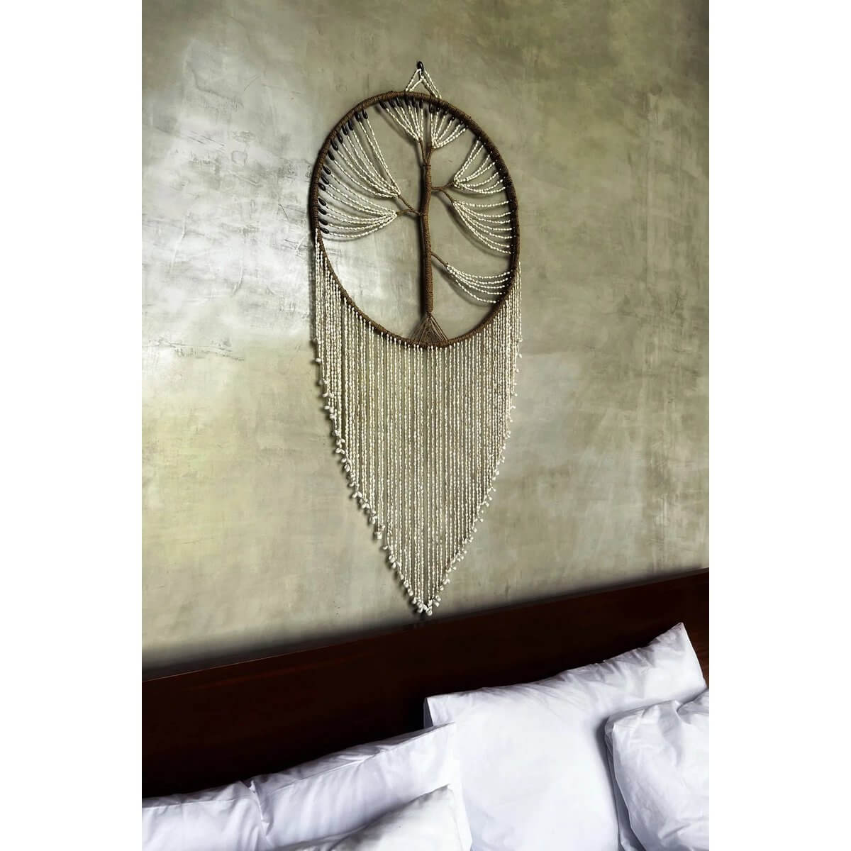 Boomvormige dromenvanger met schelpen, hangend boven een bed, vangt negatieve dromen en verspreidt positieve vibes. Handgemaakt kunstwerk.