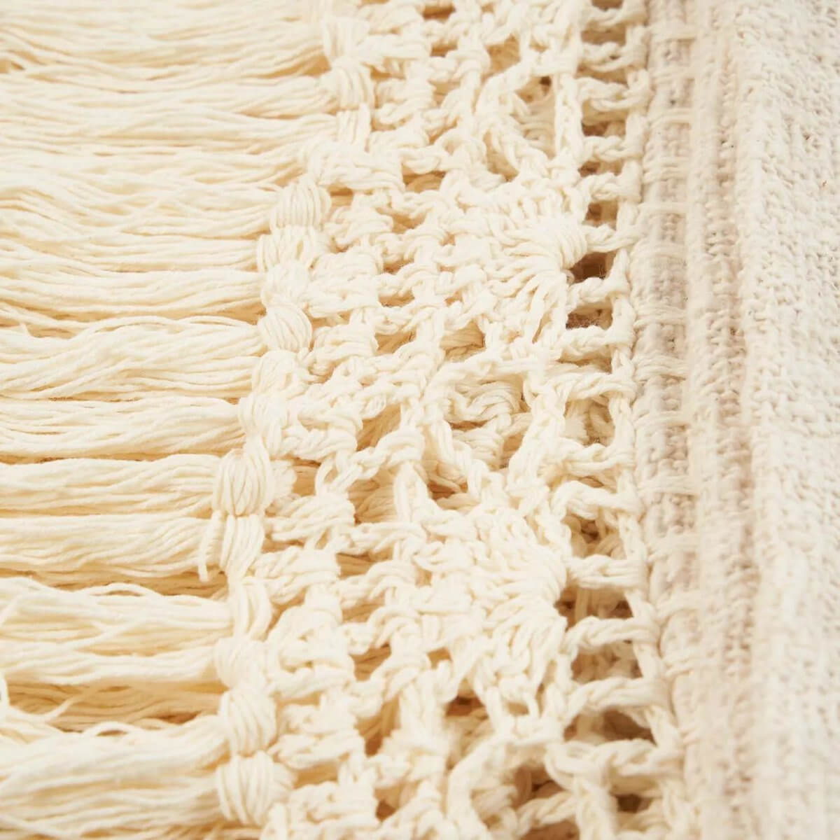 Close-up view of a natural-colored De Gypsy bedsprei with bohemian-style fringe details, adding warmth and texture to any space.