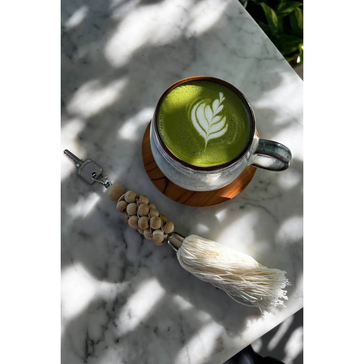 Trendy Bohemian keychain with natural white wooden beads next to a latte on a marble table, adding rustic elegance to your essentials.
