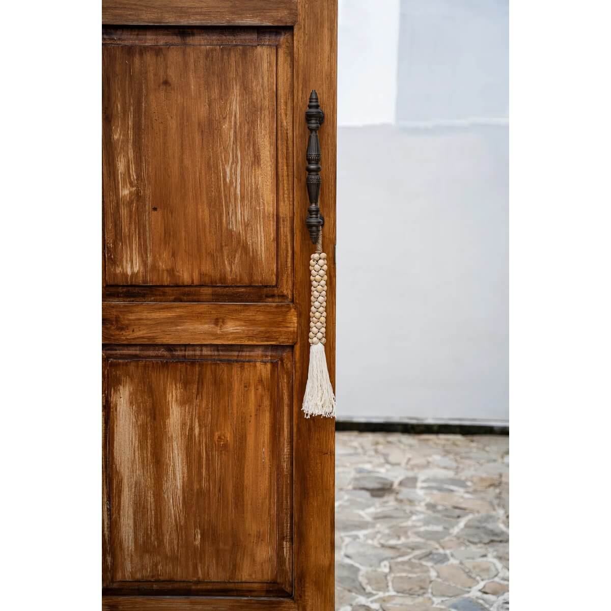 Wooden beads with cotton tassel hanging on rustic door, adding a bohemian touch to home decor.