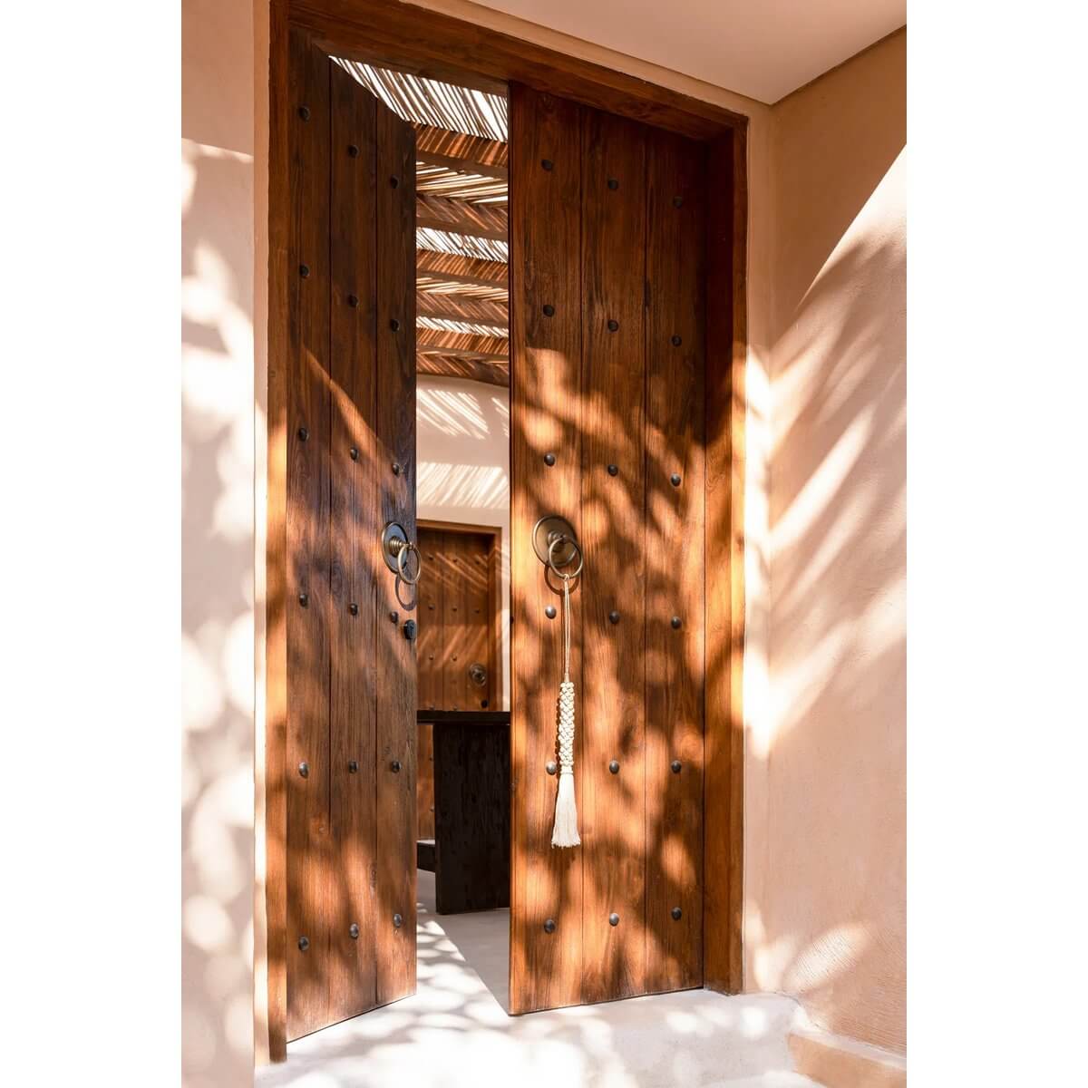 Bohemian natural white wooden beads with cotton tassel hanging on rustic door, adding exotic charm to home decor. Bazar Bizar Living.