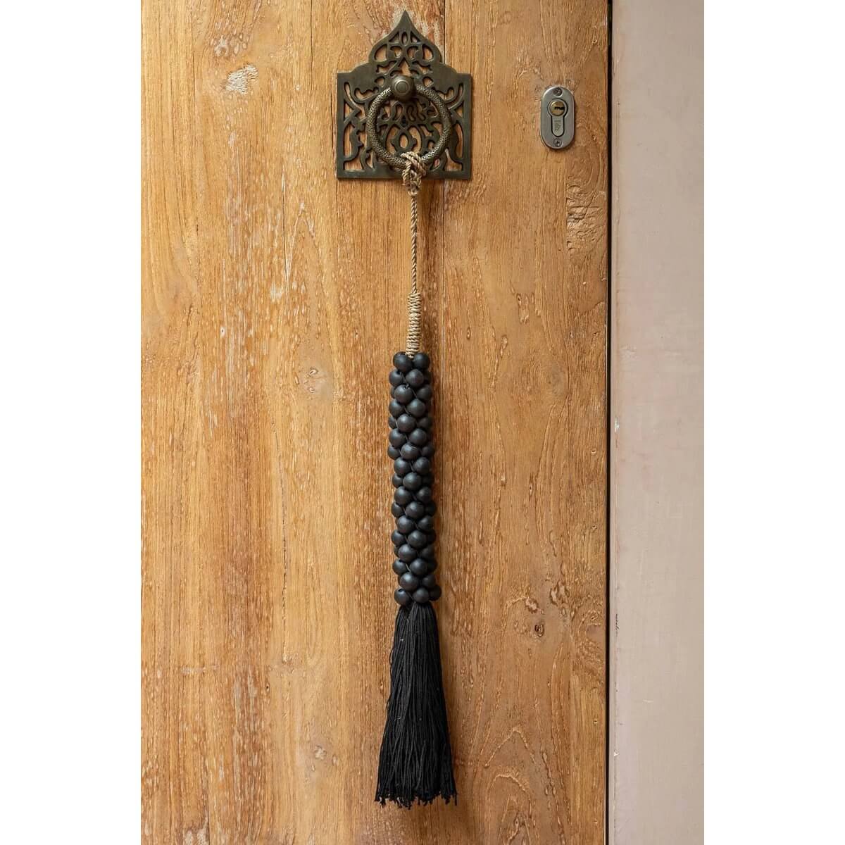 Black wooden beads with cotton tassel hanging on door, handmade bohemian decor from Bali, adds exotic charm to any home.
