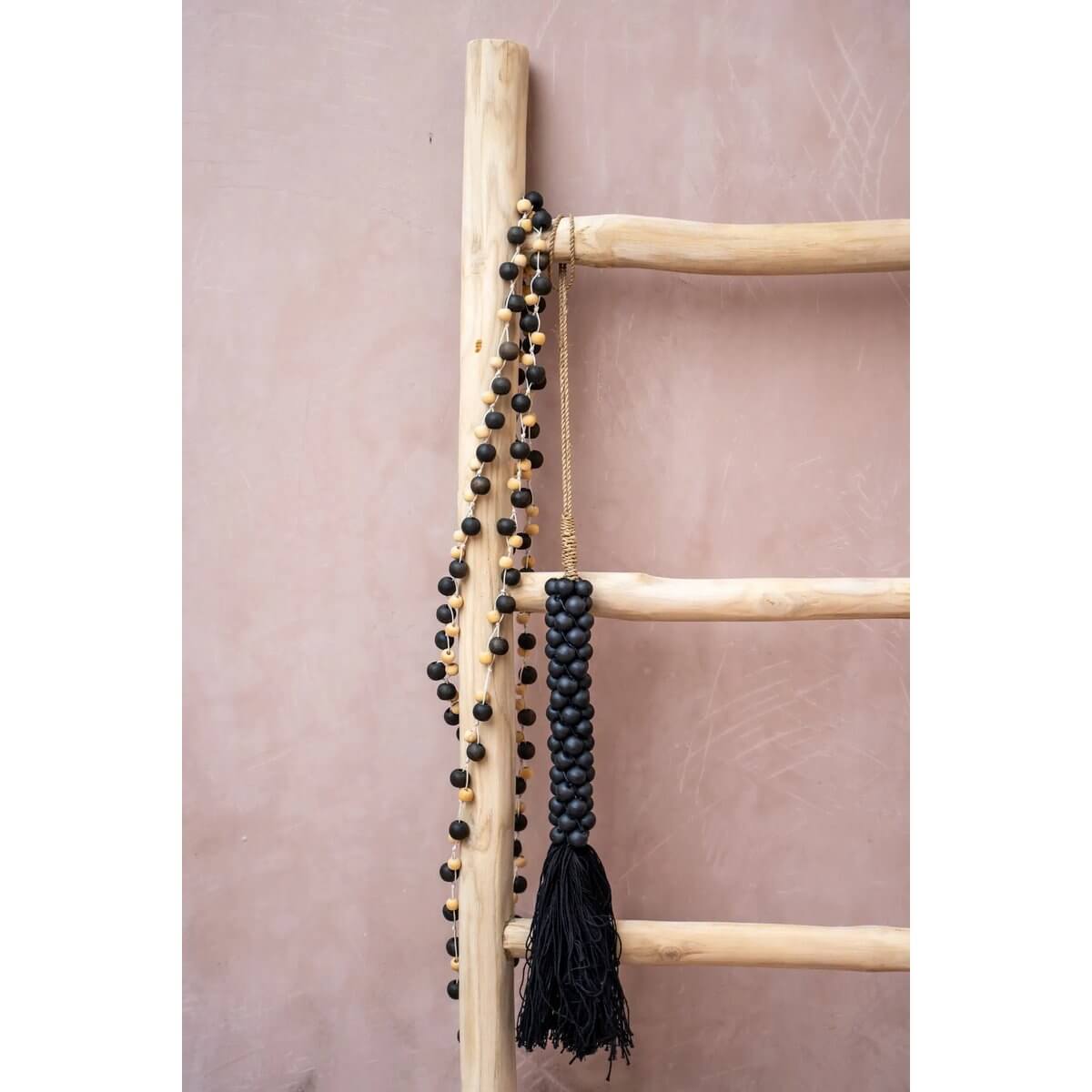 Bohemian style black wooden beads with cotton tassel hanging on a wooden ladder, handcrafted by Balinese artisans.