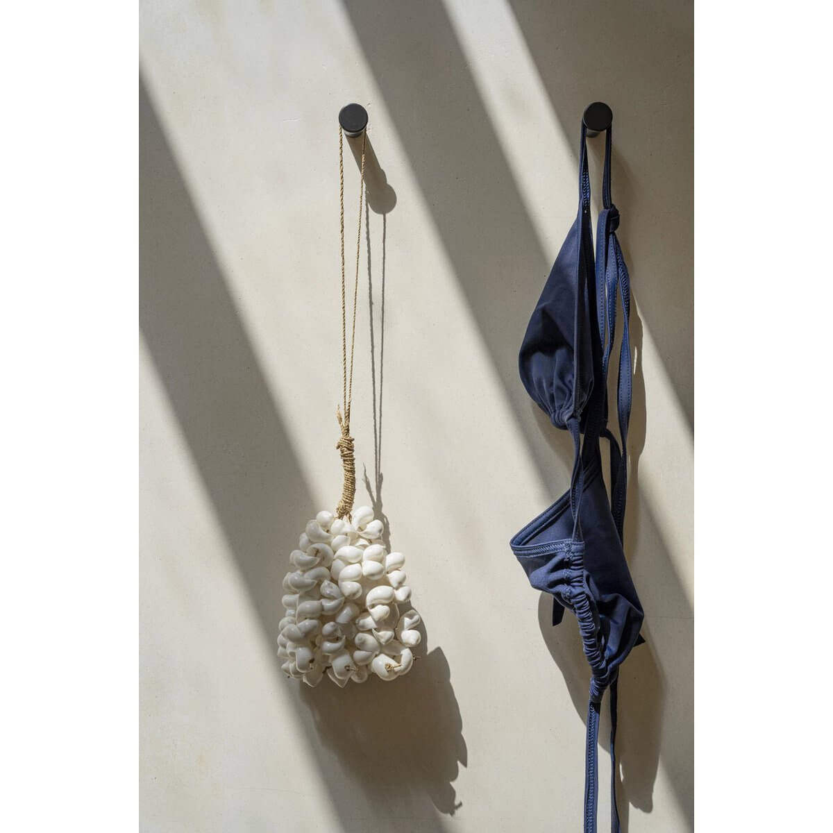 Bohemian white shell hanger handwoven by Balinese artisans, adds exotic charm to home decor, hanging next to a navy garment in sunlight.