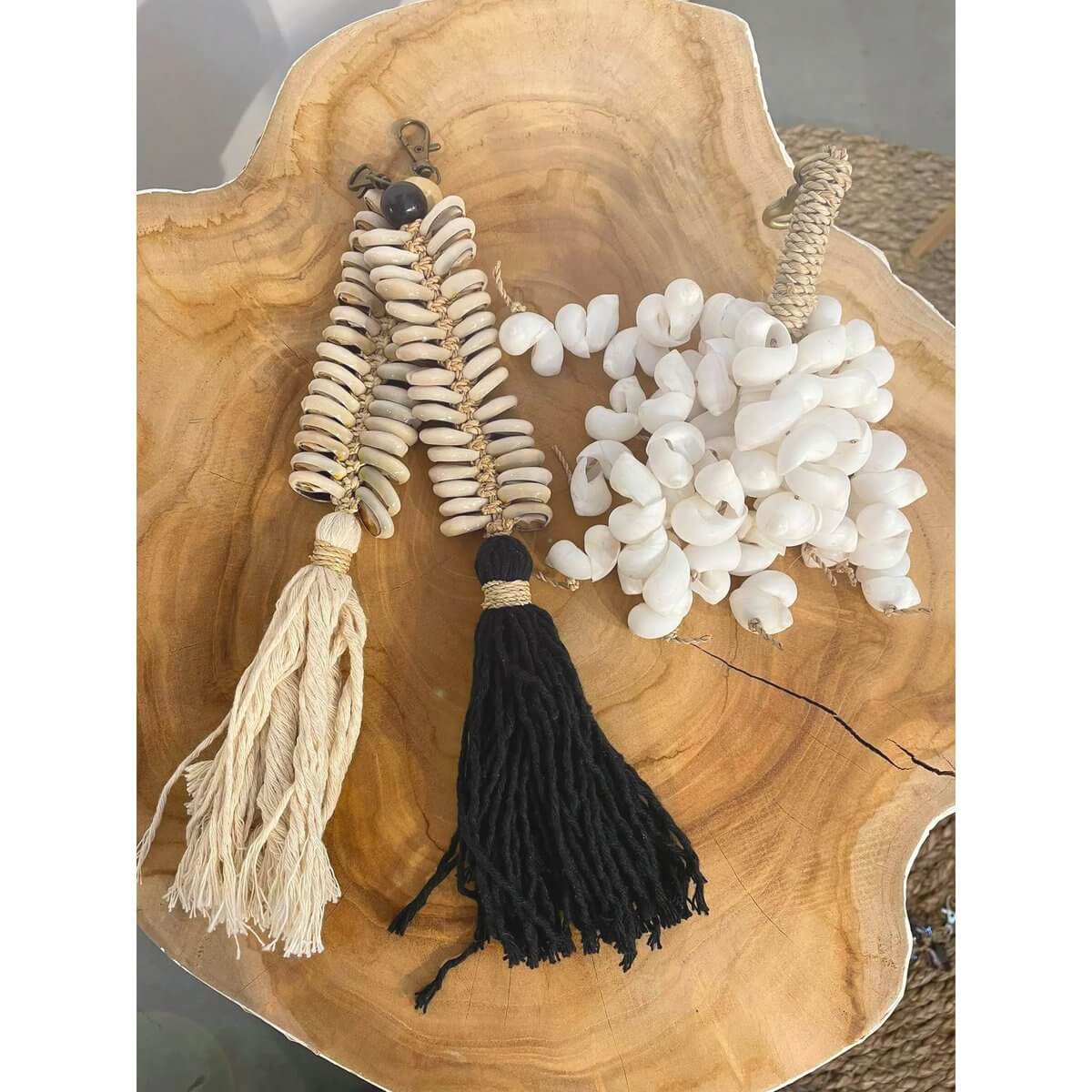 Bohemian white shell keychain with natural cotton tassels and cowrie shells on a wooden surface. Coastal elegance accessory.