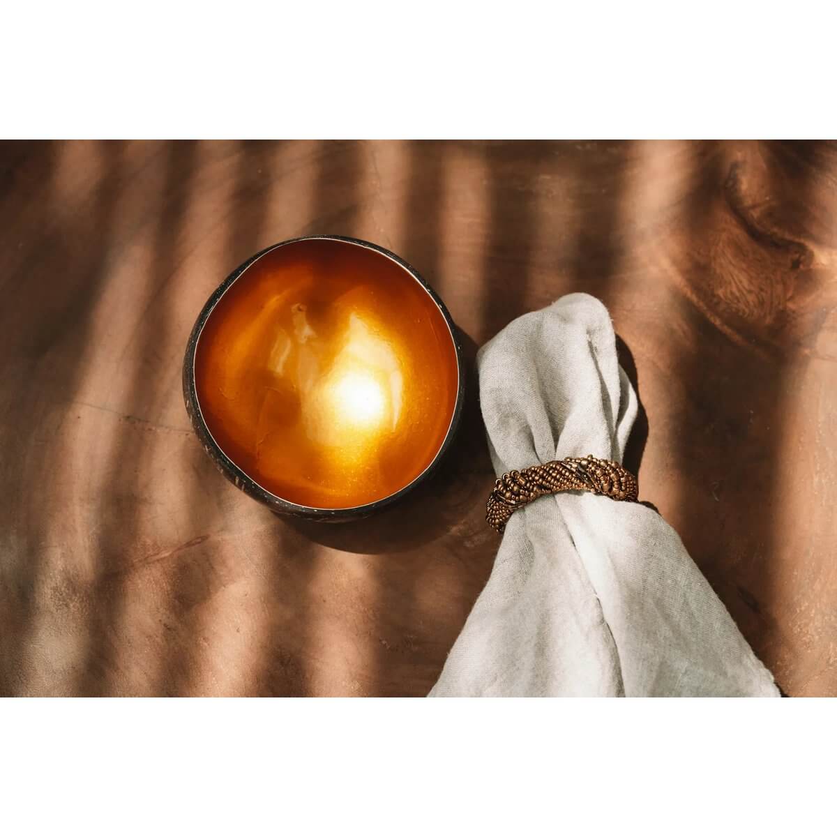 Bohemian dining setup with a gold beaded napkin ring, white napkin, and golden bowl on a wooden table.