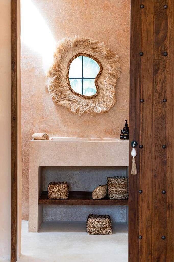 De La Principessa spiegel in natuurlijke stijl, opgehangen boven een stijlvolle badkamer met houten accenten en gevlochten manden.