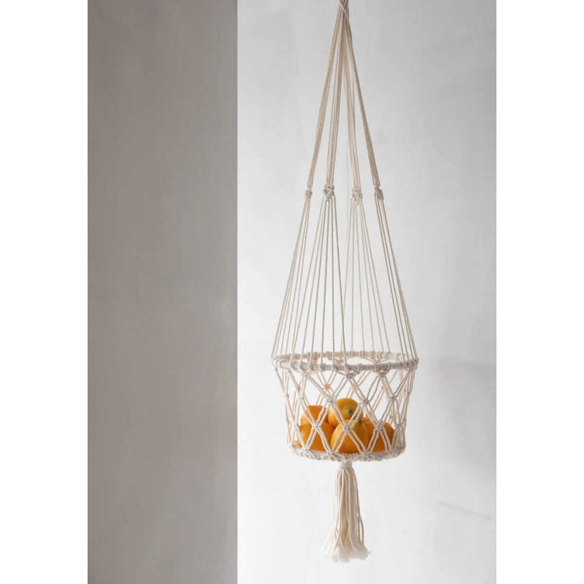 Bohemian macramé plant hanger in white holding oranges, handcrafted from cotton - perfect for indoor decor.