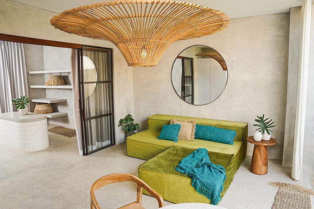 Stijlvolle woonkamer met groene bank, aquablauwe kussens en bohemian elementen, zoals een rotan hanglamp en ronde spiegel.