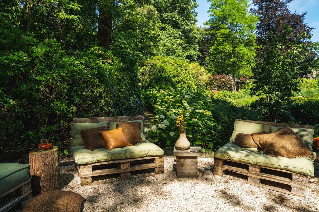Gezellige tuinset met groene tuinkussens en bruine kussenhoezen in een natuurlijke omgeving vol groen. Perfect voor een boho-stijl tuin.