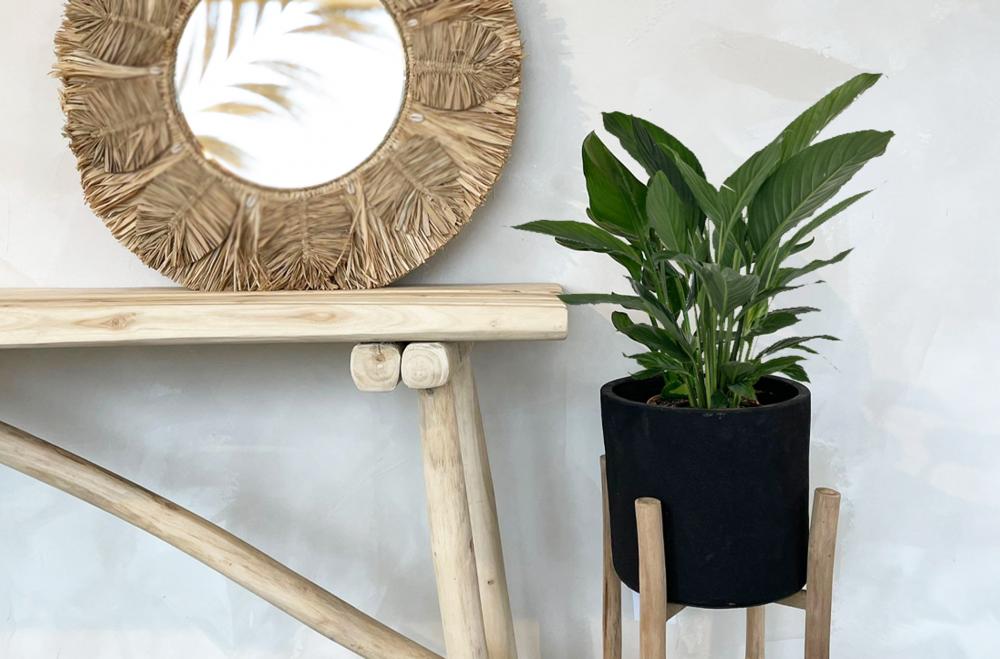 Rotan palmspiegel met raffia en kaurischelpen naast houten tafel en groene plant, perfect voor bohemian interieurstijl.