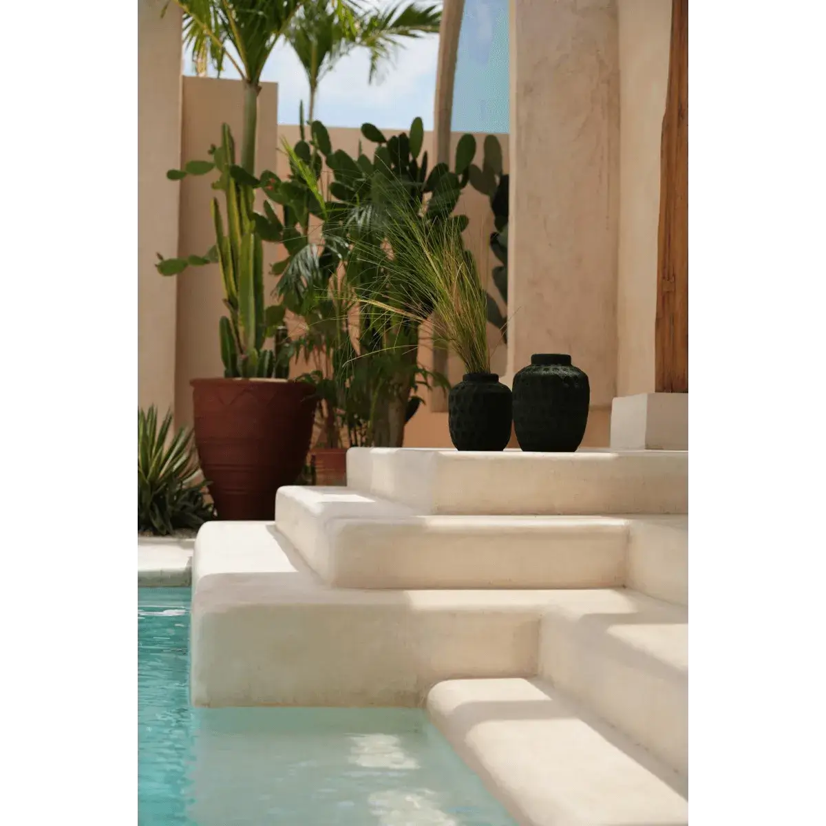 Bohemian-style garden with steps featuring two black Peaky vases, surrounded by tropical plants and a serene pool.