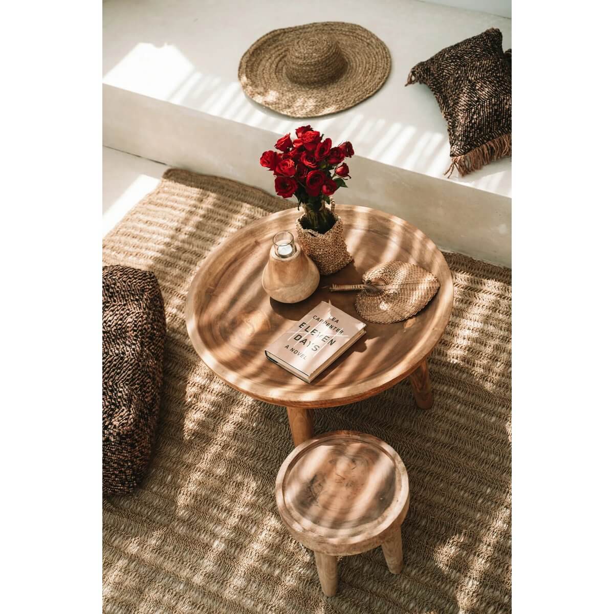 Cozy bohemian living room scene with a natural fiber hat, round wooden table, red roses, and woven decor.
