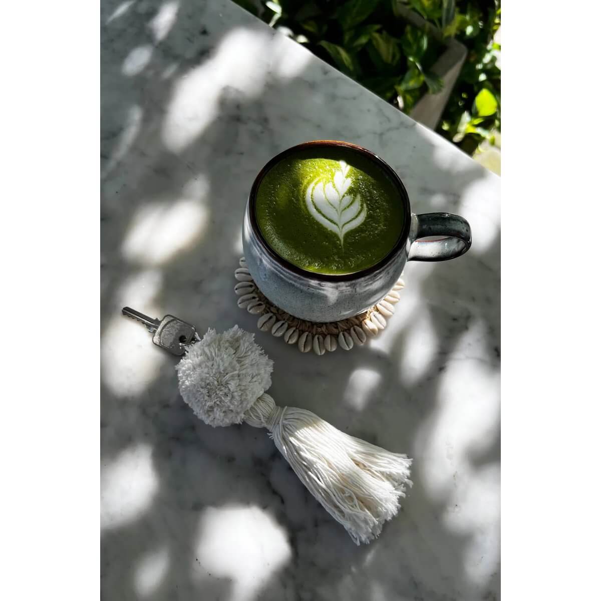 Alt Tag: Bohemian white pompom keychain next to a latte art matcha on a marble table.