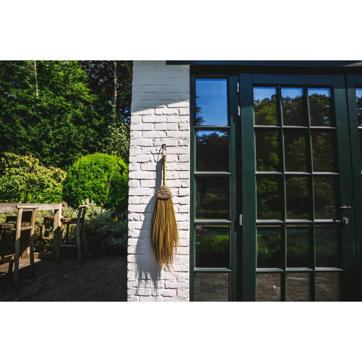 Bohemian Indonesian raffia broom hanging decoratively on exterior wall, adding natural charm to outdoor space.