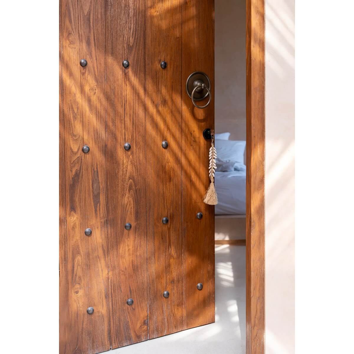 bohemian-style De Raffia Fishbone Keychain in natural white hanging on a wooden door, casting charming rustic shadows across the floor