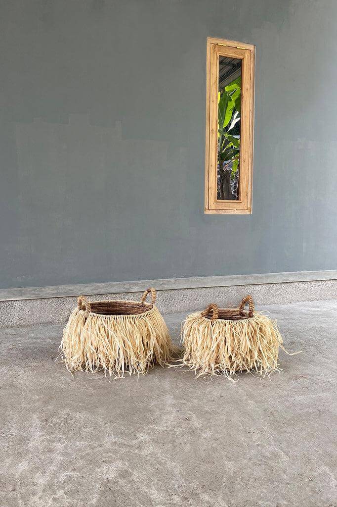 Tropische manden van raffia en bananenblad, verkrijgbaar in twee maten, staan naast elkaar tegen een grijze achtergrond.