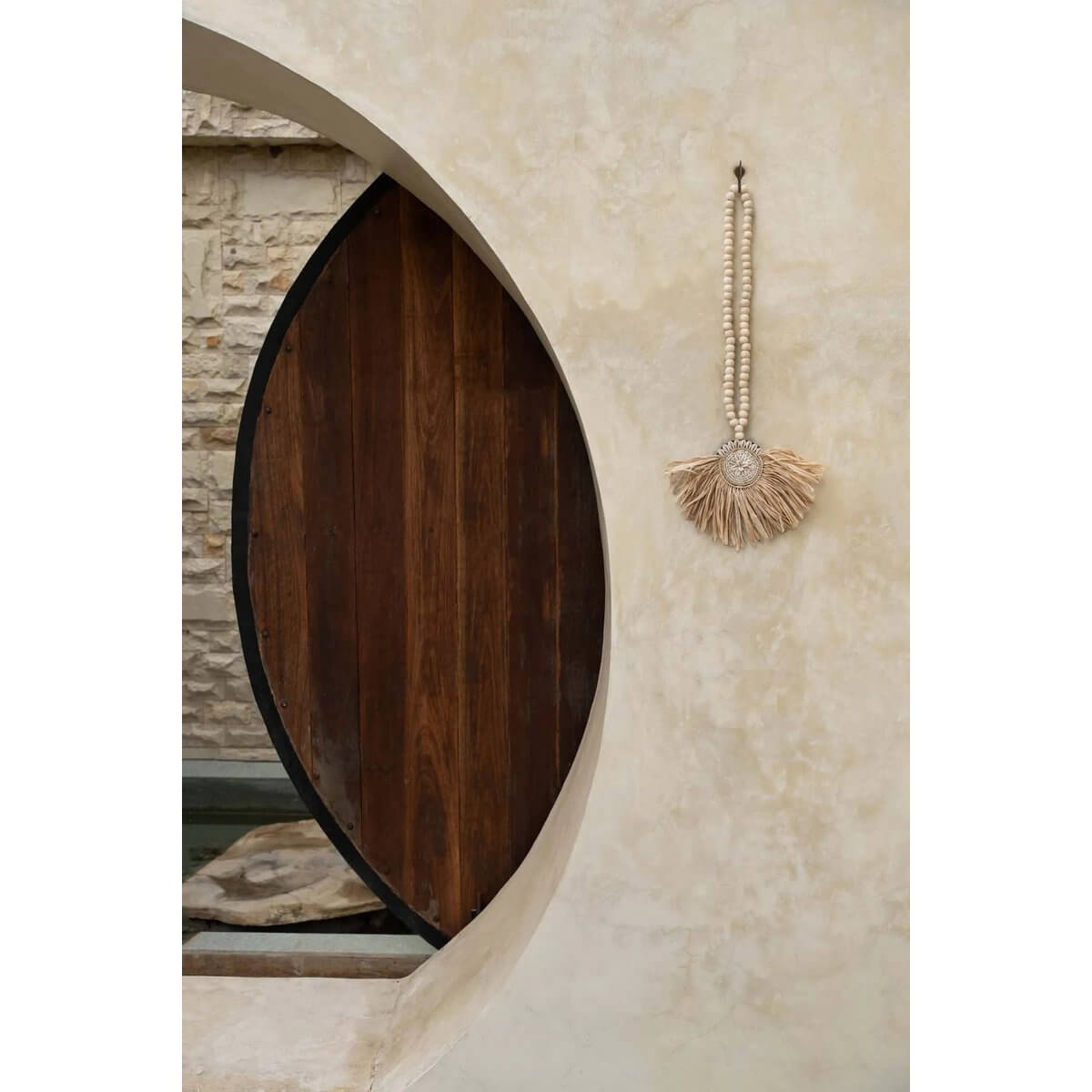 Handmade Bohemian raffia tassel hanging on a textured wall, adding a natural and rustic touch to the room.
