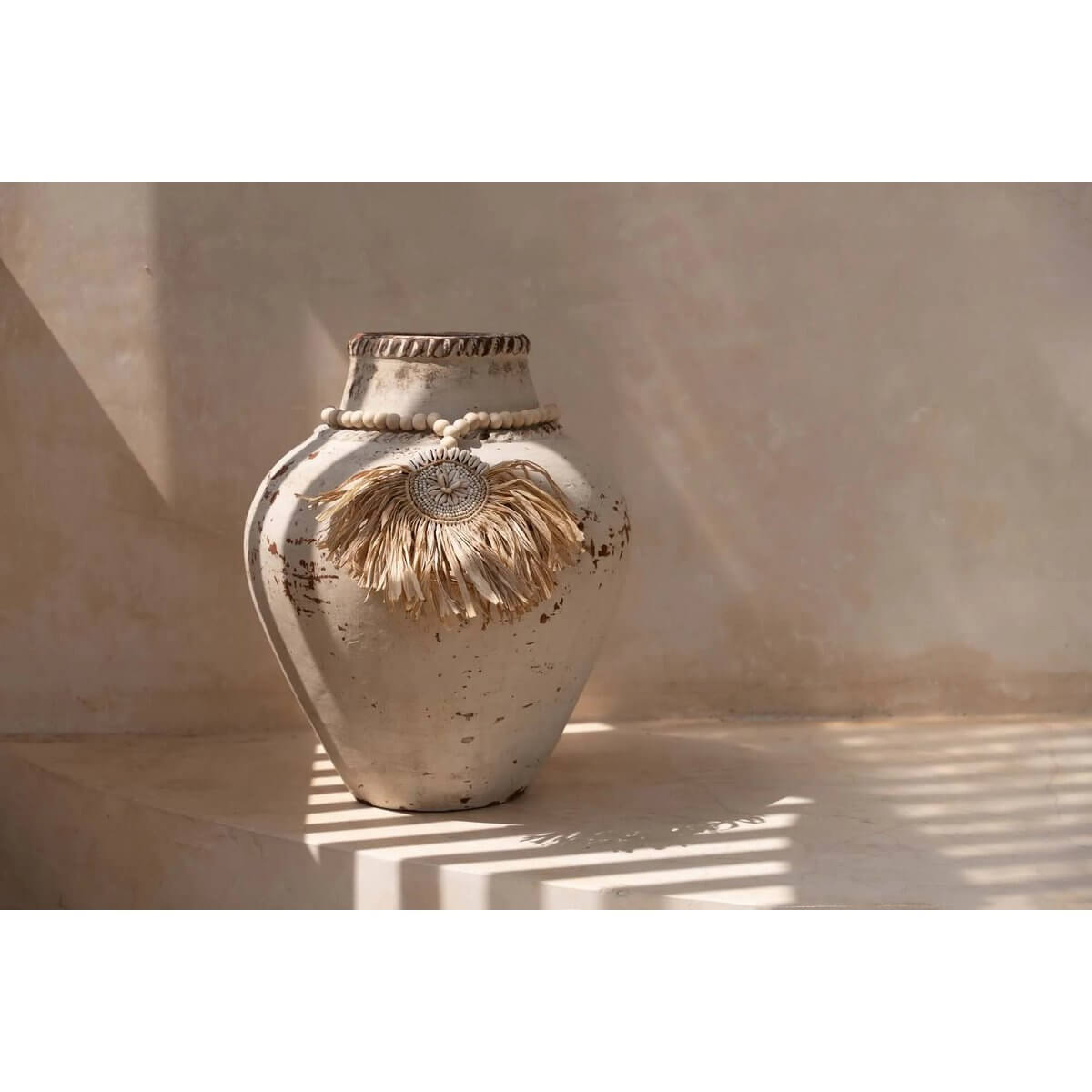 Elegant bohemian vase with natural raffia tassel, casting soft shadows in warm light.