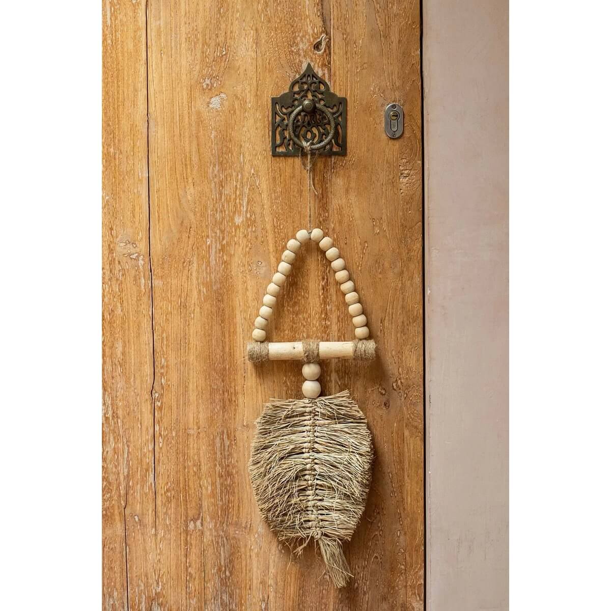 Bohemian raffia ornament hanging on wooden door, handmade by Balinese artisans, adds exotic charm to home decor. By Bazar Bizar Living.