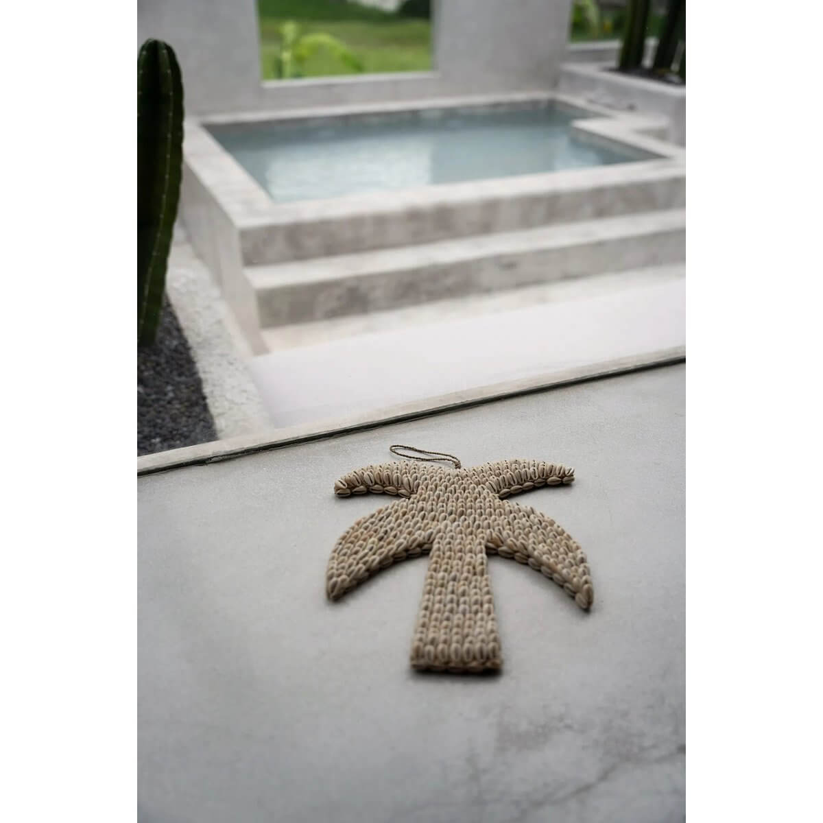 Bohemian shell palm tree decoration from Bazar Bizar Living, handcrafted in Bali, near a modern outdoor pool.
