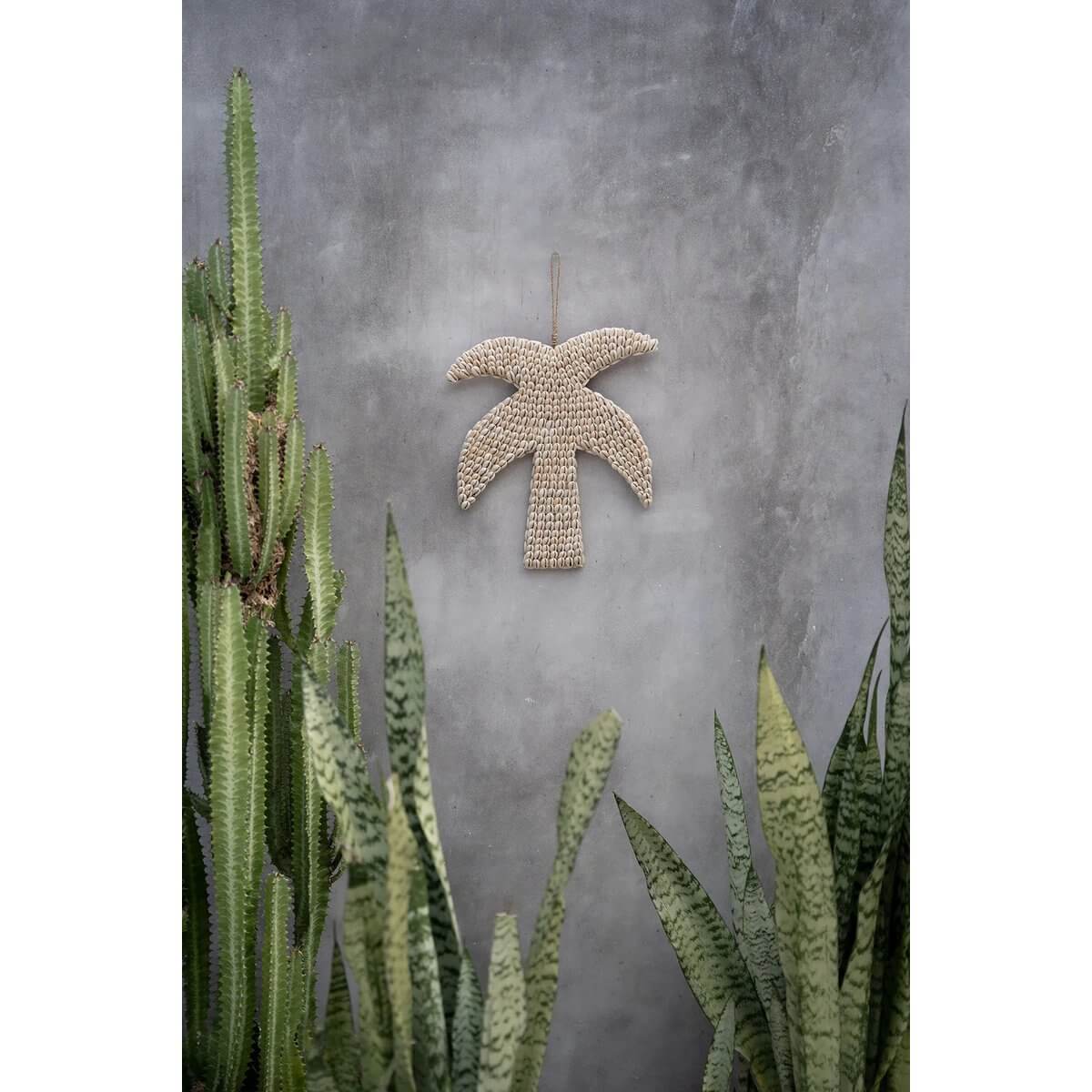 Bohemian shell palm tree decor wall hanging in tropical setting with green plants, handmade by locals in Bali.