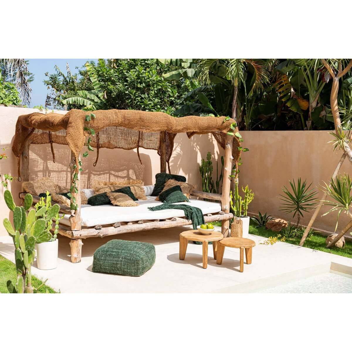 Stijlvol buitenbed met houten frame, omringd door tropische planten, naast twee Seseh salontafels op een zonnig terras.