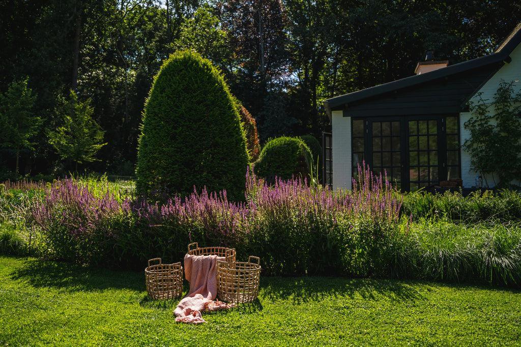 Zalm roze handgeweven katoenen plaid met franjes in een tuin, sfeervolle aanvulling voor uw interieur.