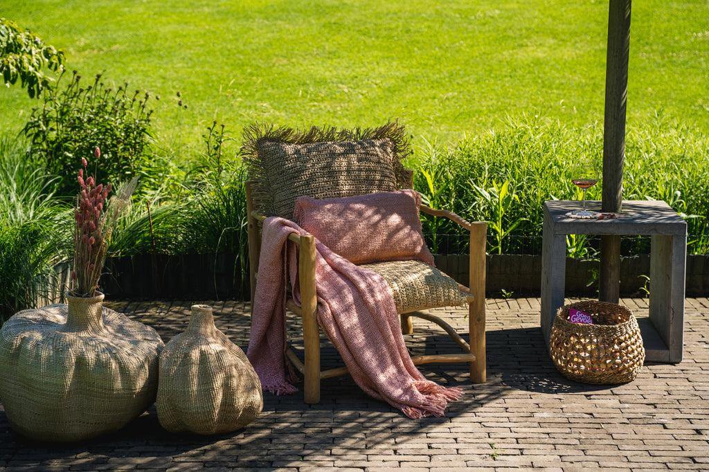Alt Tag: Luxe zalmroze handgeweven katoenen plaid met franjes op een buitenstoel in een zonnige tuin, perfecte sfeer voor frisse avonden.