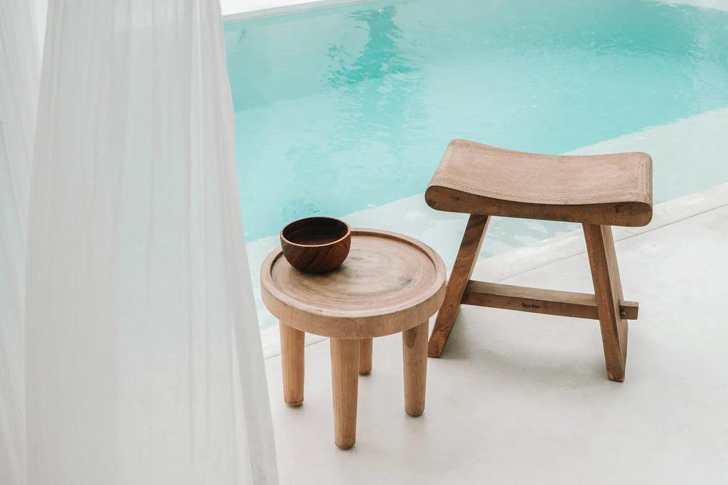 Stijlvolle houten bijzettafel en kruk naast een zwembad, perfect voor boho inrichting.