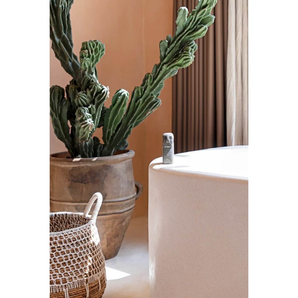 Bohemian Sumba-stone sculpture on a modern white surface, near a large potted cactus and woven basket, adding a touch of Indonesian elegance.